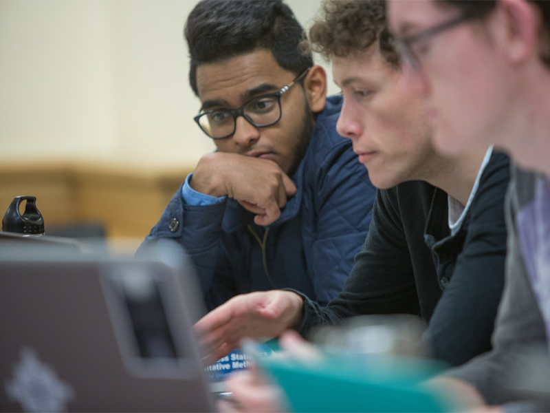 Three young men look at a shared computer