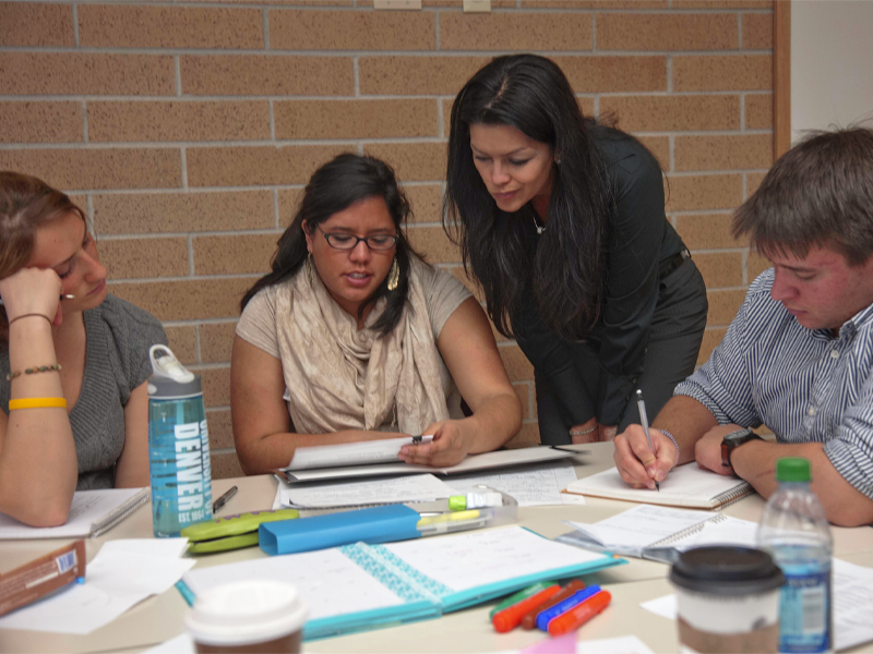 Three students working at a table while instructor consults with middle student.