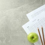 Pencils and apple on top of paper exams