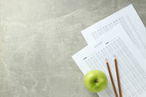 Pencils and apple on top of paper exams