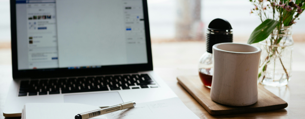 A computer, with a notebook, and a cup of coffee.