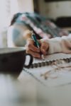 Close up photograph of a hand writing in a a notebook.