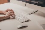 Photograph of hands typing at a computer.